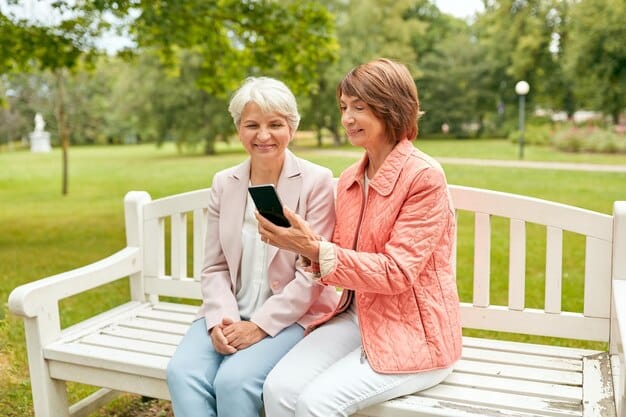 A caregiver sitting on a park bench, talking on the phone while another caregiver offers a comforting hand on their shoulder. In the background, children are playing joyfully, creating a supportive and shared atmosphere.