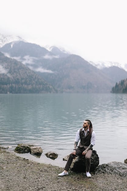 A person sitting near a lake, gazing at the tranquil water and surrounding mountains. The posture is relaxed and contemplative, conveying a sense of peace and solitude. The photo illustrates the restorative power of nature for emotional reflection and well-being.