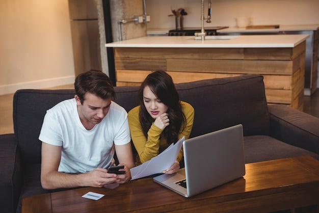A couple sitting on a couch, using a laptop to view a budget planning app. They are pointing at the screen and discussing their finances. The room is cozy and well-lit.