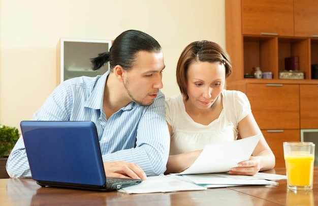 A couple sitting at a table, reviewing financial documents and using a laptop, signifying financial planning and communication. They are discussing bills, budgets, and investments with a cooperative attitude.