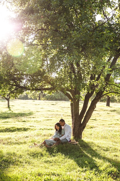 A couple sitting in a park, facing each other. The woman leans in attentively. The park is full of greenery, and the sunlight is soft, creating a peaceful and serene atmosphere.