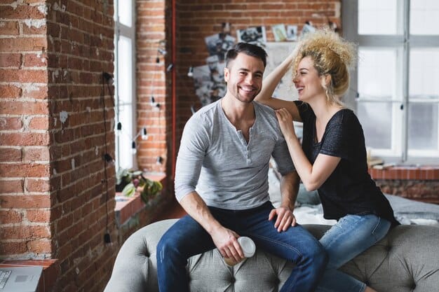 A couple sitting close together on a couch, looking at each other and smiling, representing emotional intimacy and connection.