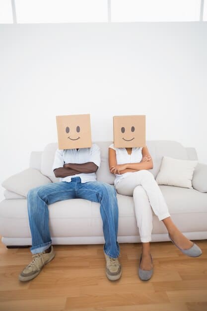 A couple sitting on opposite ends of a sofa, looking in different directions, symbolizing a lack of communication and emotional disconnect.