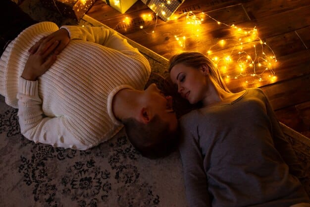 A couple sitting close together, smiling and holding hands. They are in a warmly lit room, possibly a living room or bedroom, creating a sense of intimacy and safety. The focus is on their hands and affectionate expressions, suggesting a trusting and supportive relationship.