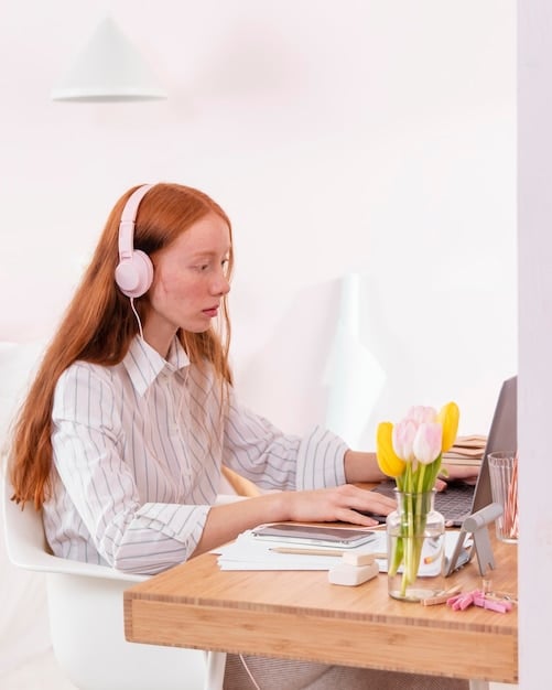 A person wearing headphones while sitting at a desk with a laptop in a brightly lit room, focused on learning through an online course platform.