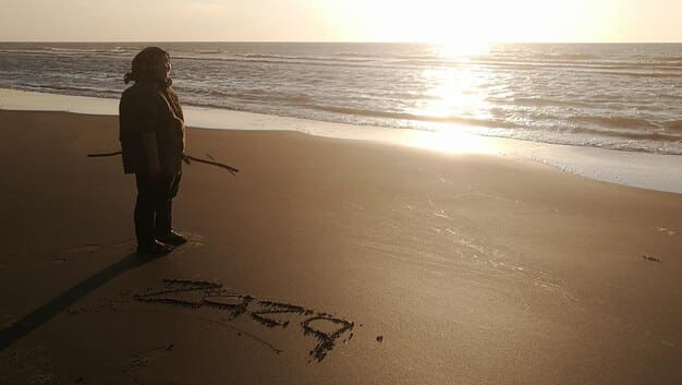 A person drawing a line in the sand, symbolizing the act of setting a boundary. The scene is at a beach during sunset, conveying a sense of peace and resolve.