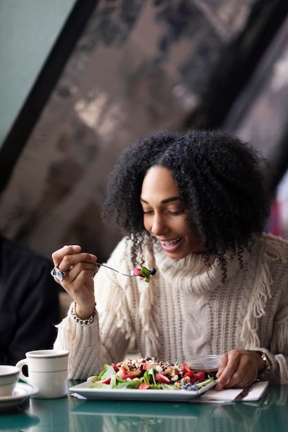 An individual sitting at a table, eating a colorful salad with evident enjoyment. The person is looking at the food with a relaxed and focused expression, and the background is softly blurred to emphasize the act of mindful eating.