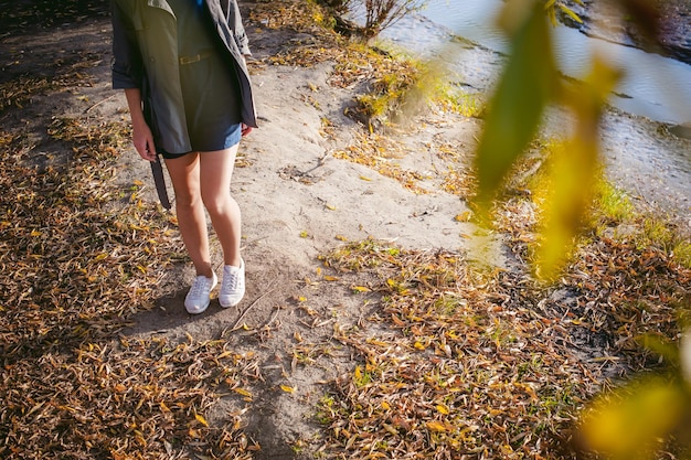Close-up of feet walking on a nature trail with sun dappling through the leaves. The image highlights the texture of the ground, the movement of the feet, and the natural light filtering through the trees, focusing on sensory details. The person's feet are wearing neutral-colored walking shoes.