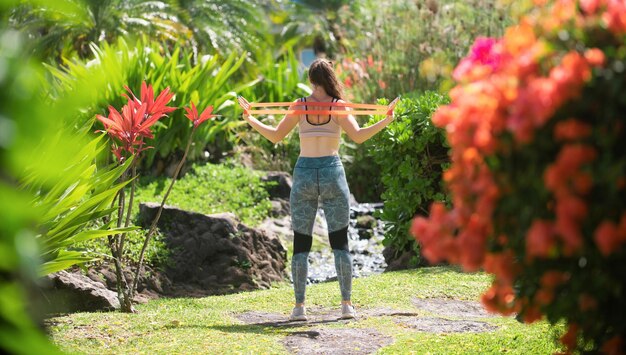 A person stretching their back in a lush garden, surrounded by greenery and colorful flowers. The pose is gentle and mindful, emphasizing the connection between physical exercise and the peaceful environment of the garden.