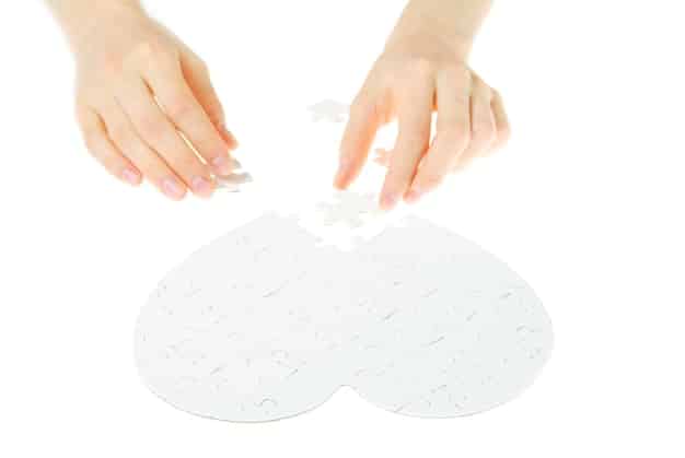 A close-up shot of a person's hand gently placing a puzzle piece into a larger, almost complete puzzle. The background is blurred, focusing on the act of careful completion and the satisfaction of fitting the piece perfectly.