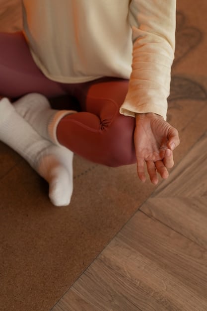 A close-up shot of a person's hands gently resting on their knees while meditating in a quiet office corner. The background is blurred, emphasizing the person's focused state. A small potted plant sits nearby, adding a touch of nature to the scene.