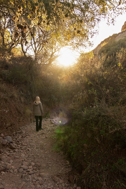 A person walking uphill on a dirt path. Their posture is straight, and they appear focused on their breathing. The environment is a lush forest with dappled sunlight.