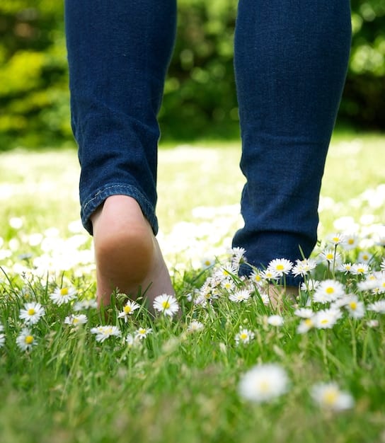 A close-up of feet walking on a grassy path. The focus is on the connection between the feet and the ground, emphasizing the sensory experience of walking.
