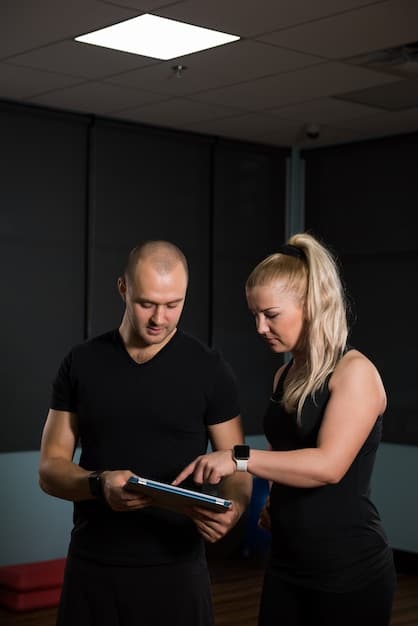 A fitness trainer guiding a client through a series of flexibility tests, ensuring proper form and safety in a brightly lit gym setting.