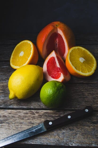 A close-up shot of a variety of citrus fruits (oranges, lemons, limes, grapefruits) sliced open, revealing their juicy interiors. Some whole fruits are also included, arranged artfully on a wooden cutting board.
