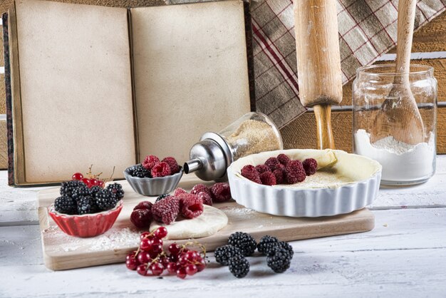 A close-up shot of a bowl of mixed berries (strawberries, blueberries, raspberries) with a light dusting of powdered sugar, set against a blurred background of a sunny kitchen.