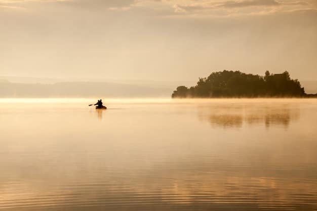 A person kayaking on a calm lake surrounded by mountains. The sun is setting, casting a warm glow over the water and the kayaker, creating a serene and peaceful atmosphere.