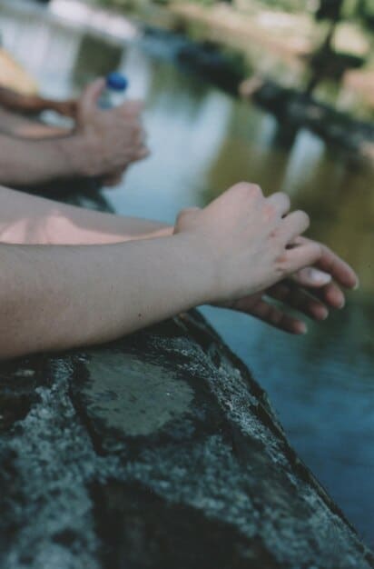 Close-up of hands gently placed on knees in a meditative pose, with a soft, blurred background of nature, emphasizing the calming and grounding aspects of meditation and mindfulness.