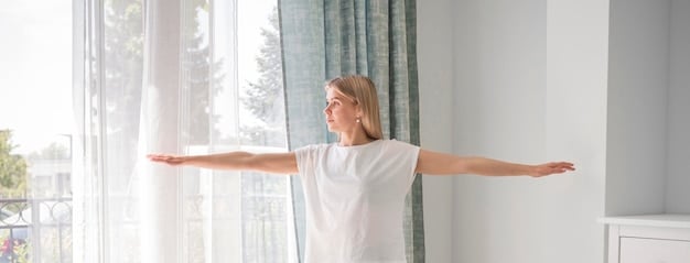 A person smiles while performing a standing side stretch with one arm extended overhead, reaching towards the opposite side. A sunny window provides soft, natural light.