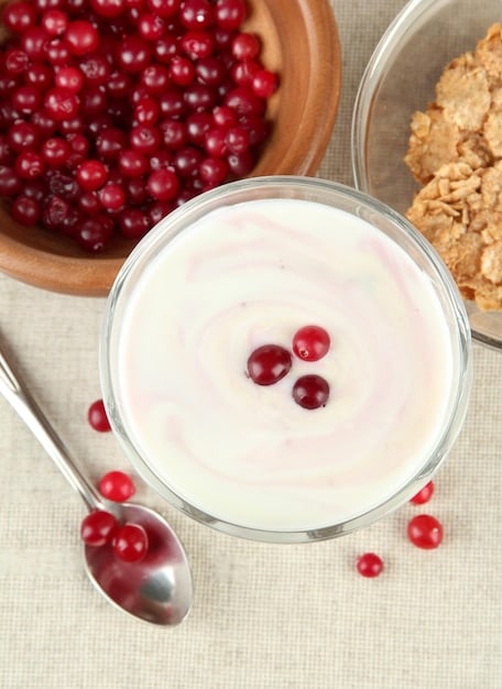 A glass bowl filled with creamy Greek yogurt, generously topped with a mix of fresh, vibrant berries like blueberries, strawberries, and raspberries. A spoon rests inside the bowl, suggesting a ready-to-eat snack.