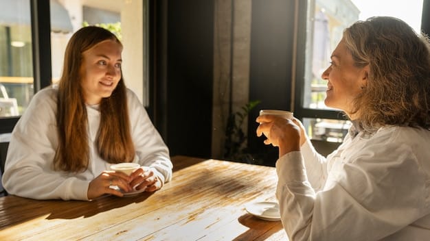 Two people having a calm and respectful conversation while seated at a table in a sunlit cafe. They are maintaining eye contact and listening attentively to each other, with relaxed body language.